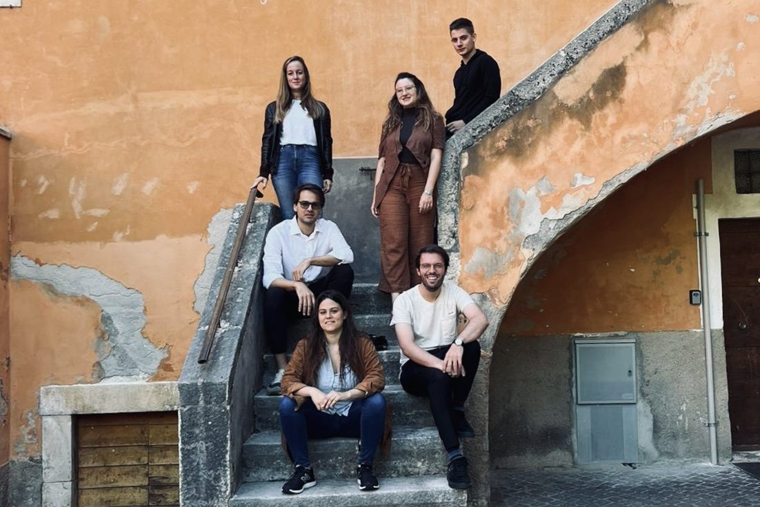 Six people posed on an external stone stair against an orange plastered wall in a historic town